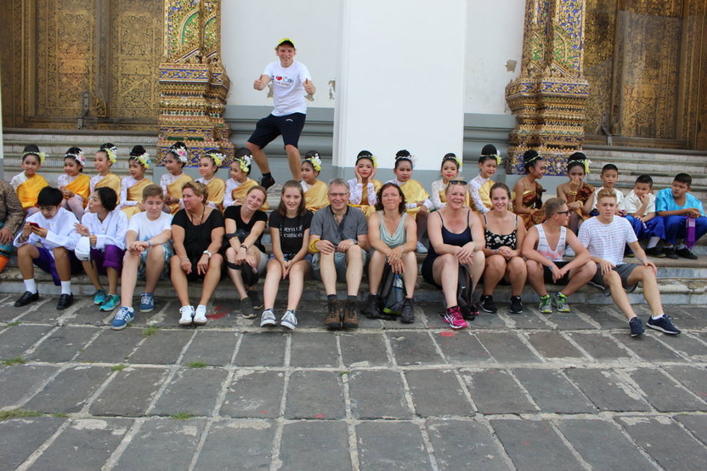 Groepsfoto tijdens familiereis Thailand bij een Thaise tempel, met dansers in traditionele kleding op de achtergrond.