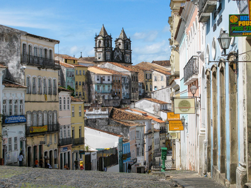 Kleurrijke koloniale straat in Salvador de Bahia, Brazilië, met historische huizen en kerktorens op de achtergrond.
