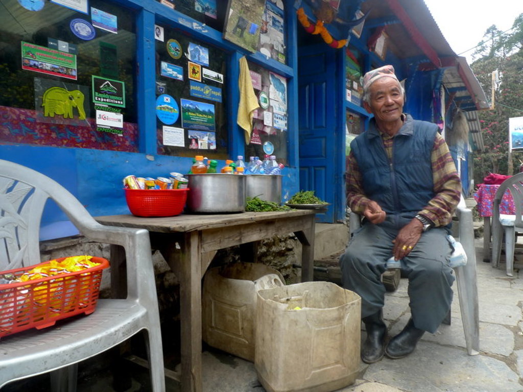 Man zit voor een theehuis in Nepal met snacks en drankjes op tafel tijdens een groepsrondreis.