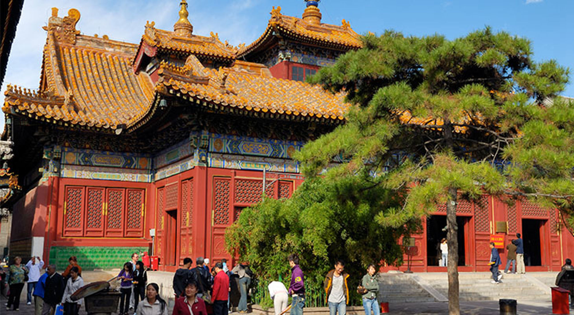 Traditionele Chinese tempel met rood gebouw en gouden dakpannen, met bezoekers op het plein.