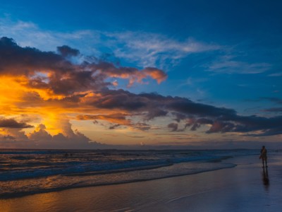 Zonsondergang aan het strand in India, met golven en een wandelaar langs de kust.