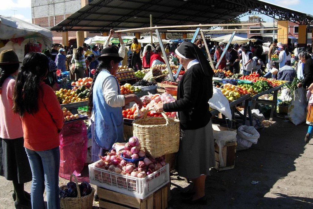 Lokale markt met rieten dak in Ecuador tijdens groepsrondreis, met kraampjes en bezoekers.