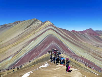 Bezoekers op de Regenboogberg Vinicunca in Peru, met kleurrijke berglagen onder een heldere blauwe lucht.