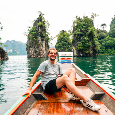 Man zit in een longtailboot op een groen meer tussen kalkstenen rotsen in Thailand tijdens een 22-35ers reis.