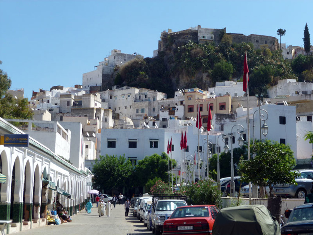 Witte huizen in Chefchaouen, Marokko, met rode vlaggen langs de straat en een fort op de heuvel.