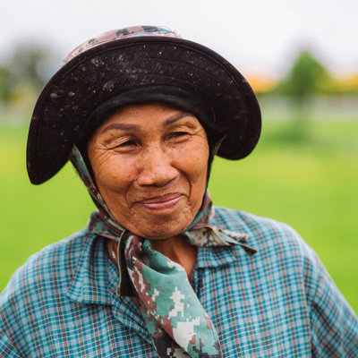 Portret van een Thaise rijstboerin met hoed en sjaal in een groen rijstveld tijdens groepsrondreis Thailand.