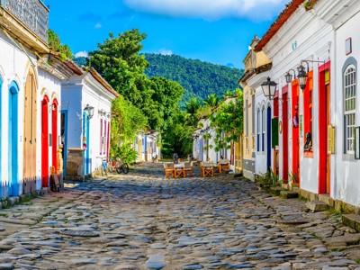 Kleurrijke koloniale straat met kinderkopjes in Paraty, Brazilië, met groene heuvels op de achtergrond.