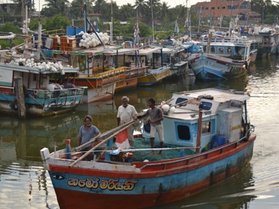 Vissersboot in de haven van Negombo, Sri Lanka, met kleurrijke boten op de achtergrond.