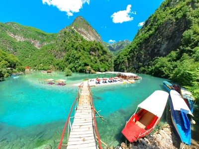 Houten brug naar strandje aan helderblauw meer in de bergen, route Albanië, Kosovo & Noord-Macedonië.