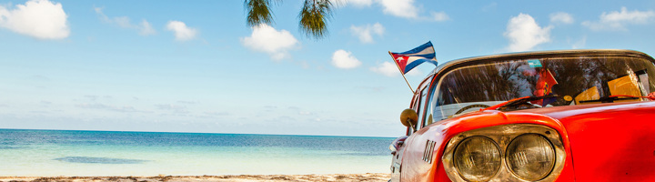 Rode oldtimer met Cubaanse vlag aan het strand, passend bij singlereizen Cuba.