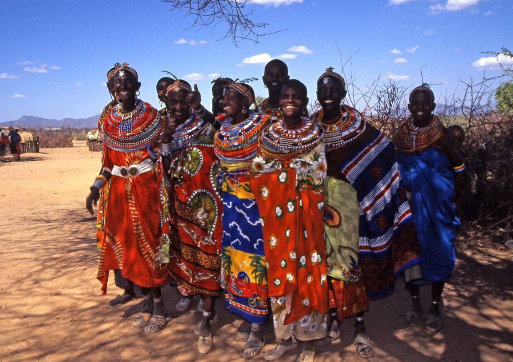 Vrolijke Samburu-vrouwen in kleurrijke kleding langs een zandweg tijdens groepsrondreis Kenia, Tanzania en Zanzibar.
