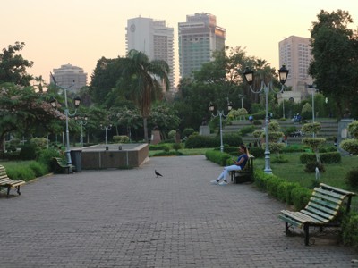 Park in Caïro met wandelpad, bankjes en skyline bij zonsondergang.