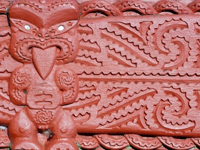 Rood geschilderd Maori houtsnijwerk met traditionele patronen, Route Nieuw-Zeeland.