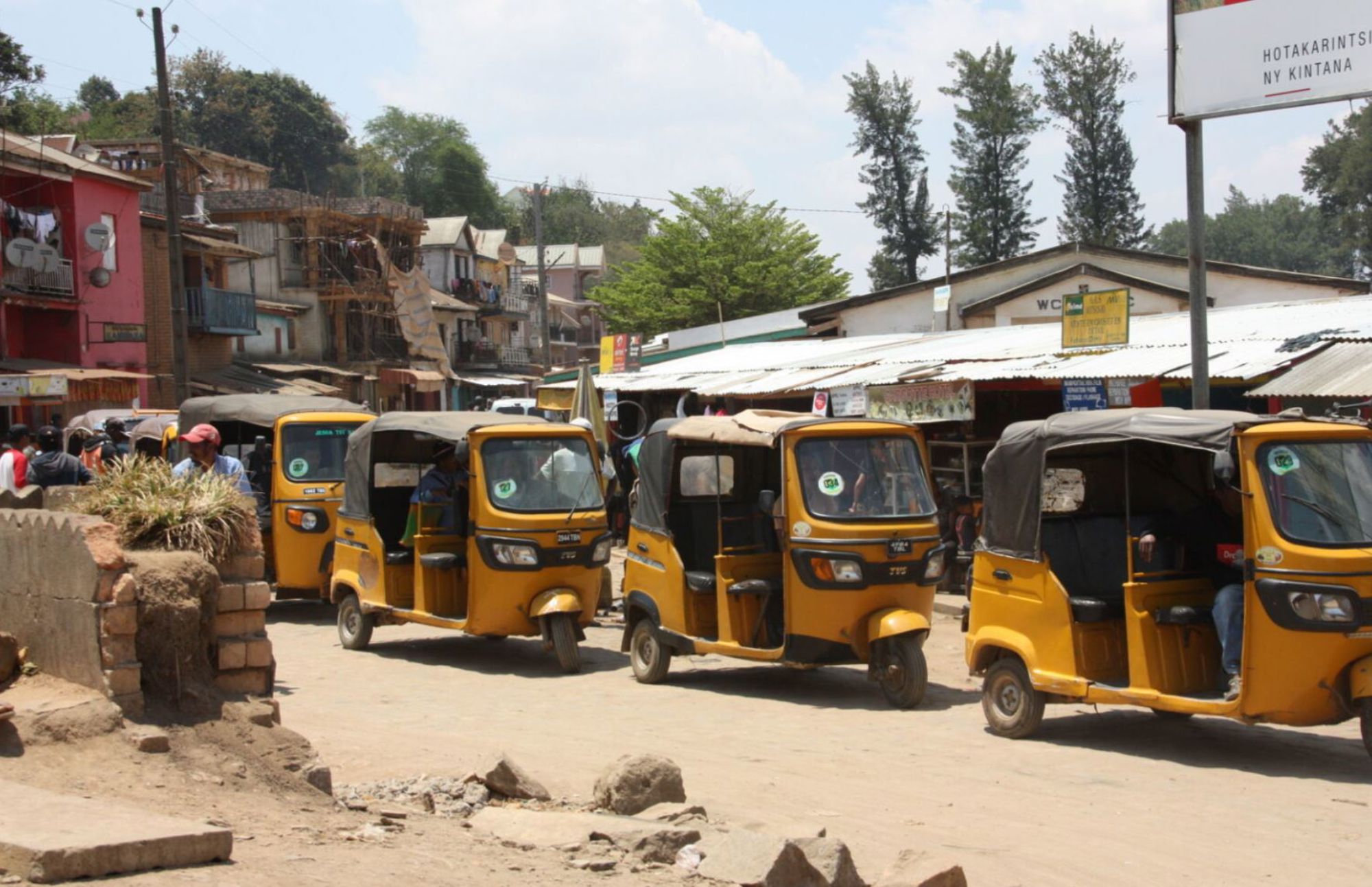 Rij gele tuktuks op een drukke straat in Madagascar, met marktkraampjes en gebouwen op de achtergrond.