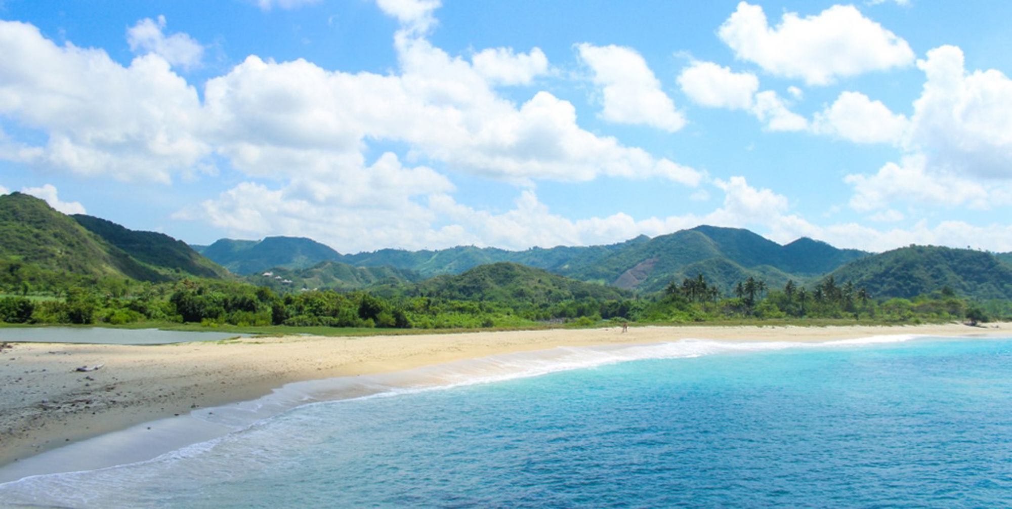 Tropisch zandstrand met turquoise zee en groene heuvels op de achtergrond in Indonesië.