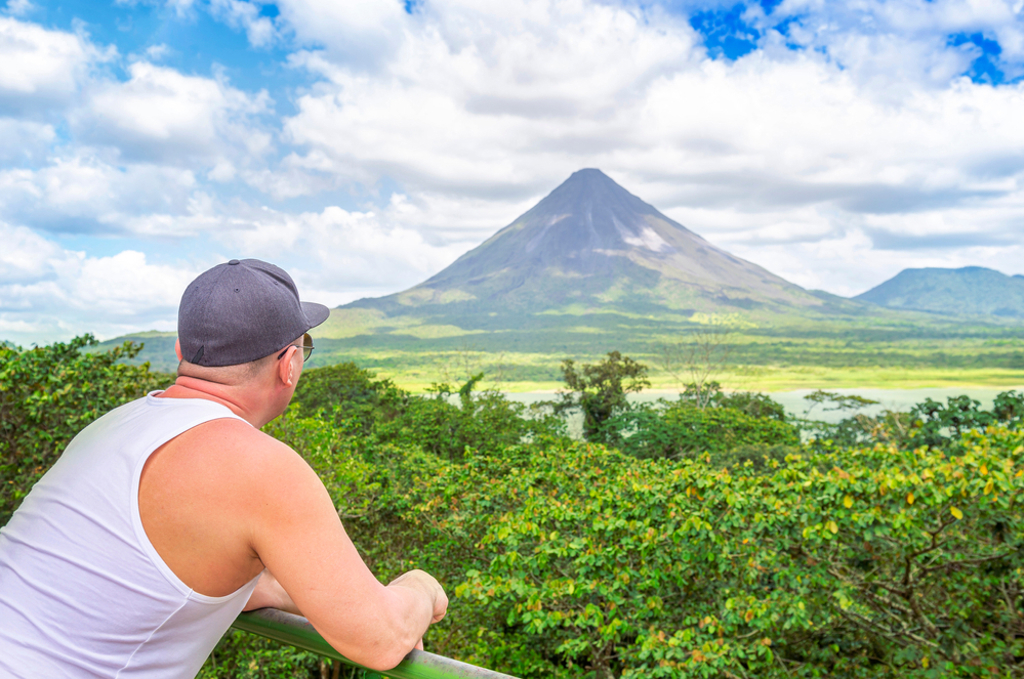Reiziger kijkt uit over het groene landschap met de Arenal-vulkaan tijdens groepsrondreis Trans-Midden-Amerika.