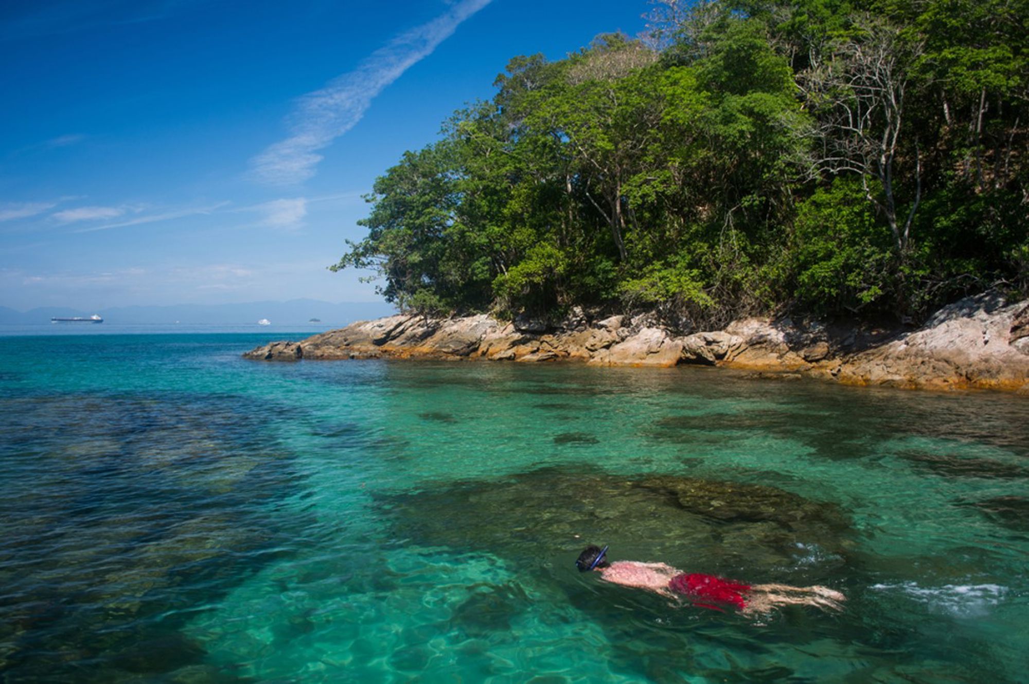 Snorkelaar in helderblauw water bij een groen, rotsachtig eiland aan de kust van Brazilië.