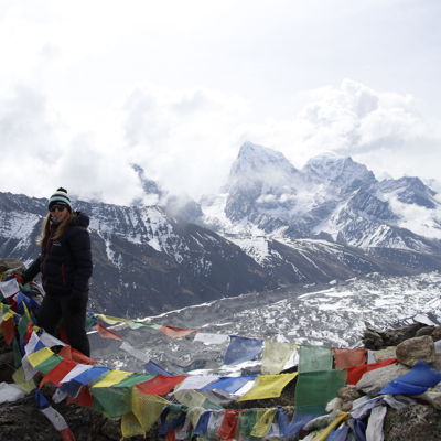 Wandelaar bij gebedsvlaggen met uitzicht op besneeuwde Himalaya-toppen tijdens groepsrondreis Nepal Everest.