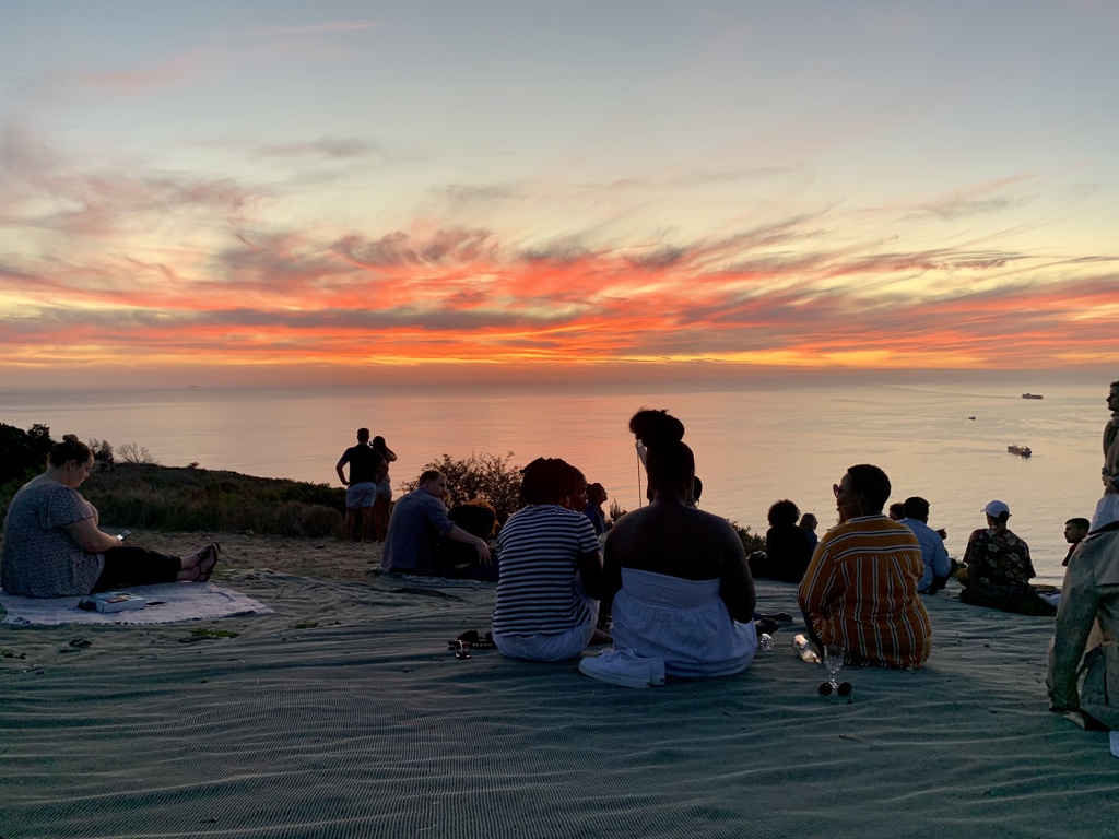 Reizigers kijken bij zonsondergang uit over de oceaan tijdens een 22-35ers reis door Zuid-Afrika.