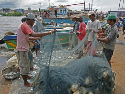 Vissers halen het net binnen bij de haven in Sri Lanka, met boten op de achtergrond.