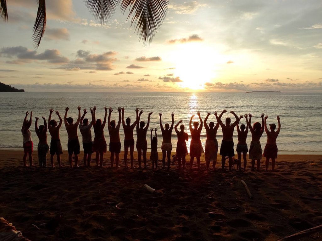 Groep reizigers met opgeheven armen op het strand bij zonsondergang in Costa Rica tijdens een familiereis.