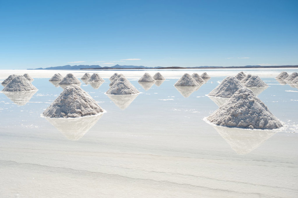 Zoutkegels op de Salar de Uyuni zoutvlakte in Bolivia, met spiegelende waterlaag en bergen in de verte.