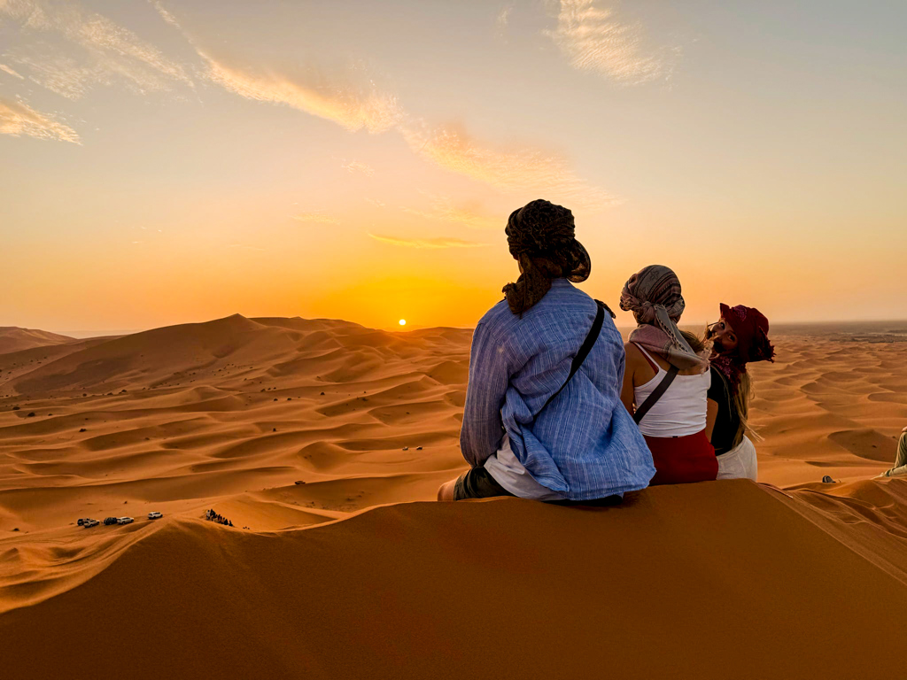 Gezin met lokale gids kijkt uit over de Sahara-duinen bij zonsondergang tijdens een familiereis in Marokko.