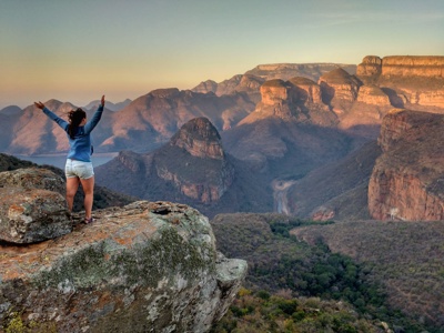 Uitzicht over Blyde River Canyon langs de Route Zuid-Afrika, met reiziger op rots bij zonsopkomst.