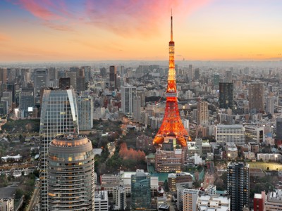 Tokyo Tower verlicht bij zonsondergang, met skyline van Tokio op de achtergrond.
