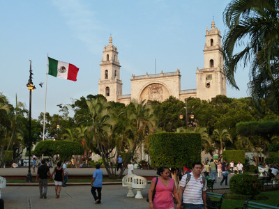 Kathedraal van Mérida aan het centrale plein met de Mexicaanse vlag en wandelende bezoekers.