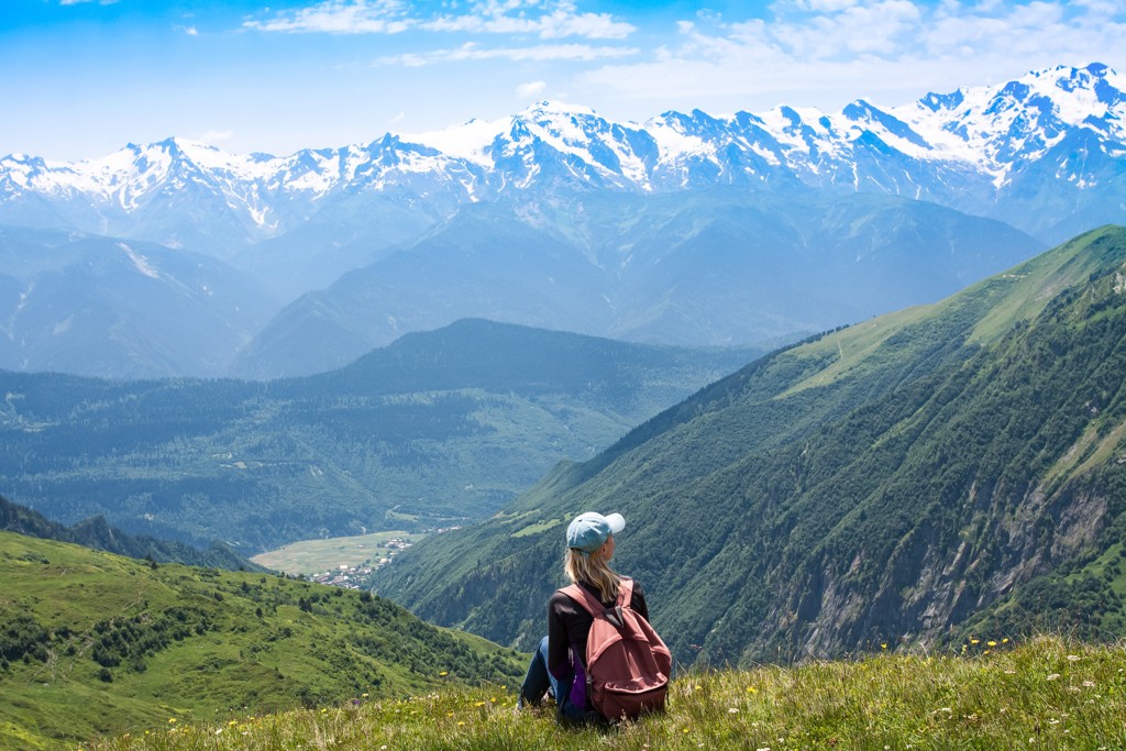 Jonge reiziger met rugzak kijkt uit over groene bergen en besneeuwde toppen in Georgië.