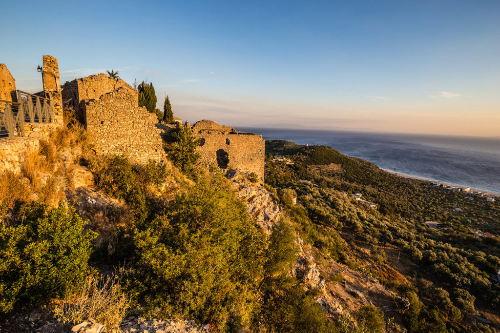 Ruïnes van een kasteel op een heuvel met uitzicht op de Albanese kust bij zonsondergang.