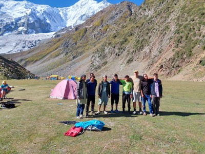 Groepsfoto bij een tentenkamp in Baltistan, met besneeuwde bergtoppen en een gletsjer op de achtergrond.