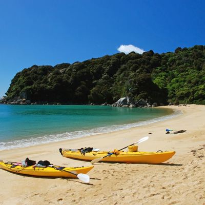 Gele kajaks op het strand bij Abel Tasman National Park, met helderblauw water en groene heuvels.