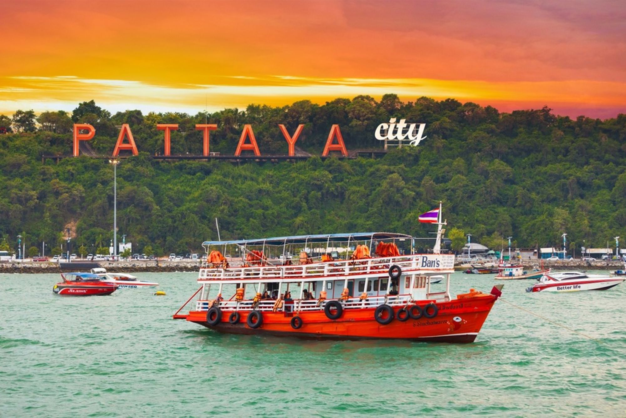 Boot op zee bij Pattaya City in Thailand, met het Pattaya-bord op de heuvel bij zonsondergang.