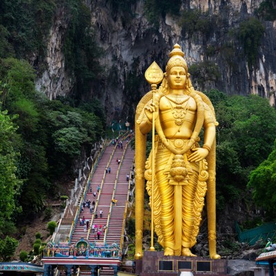 Gouden Murugan-beeld bij de Batu Caves, Maleisië, met kleurrijke trappen naar de grotten in de kalksteenrotsen.