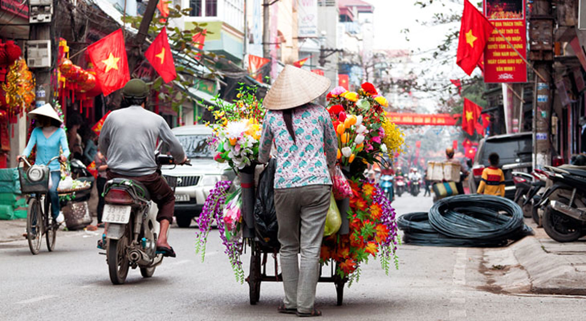 Hanoi Straatbeeld in Vietnam met bloemenverkoper op kar, scooters en Vietnamese vlaggen.