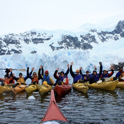 Groep kajakkers peddelt in Spitsbergen langs een gletsjer en besneeuwde bergen.