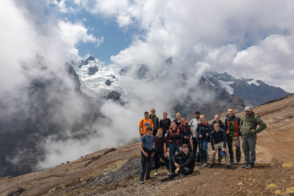 Groep 22-35ers wandelaars in de Peruaanse Andes met besneeuwde bergtoppen en wolken op de achtergrond.