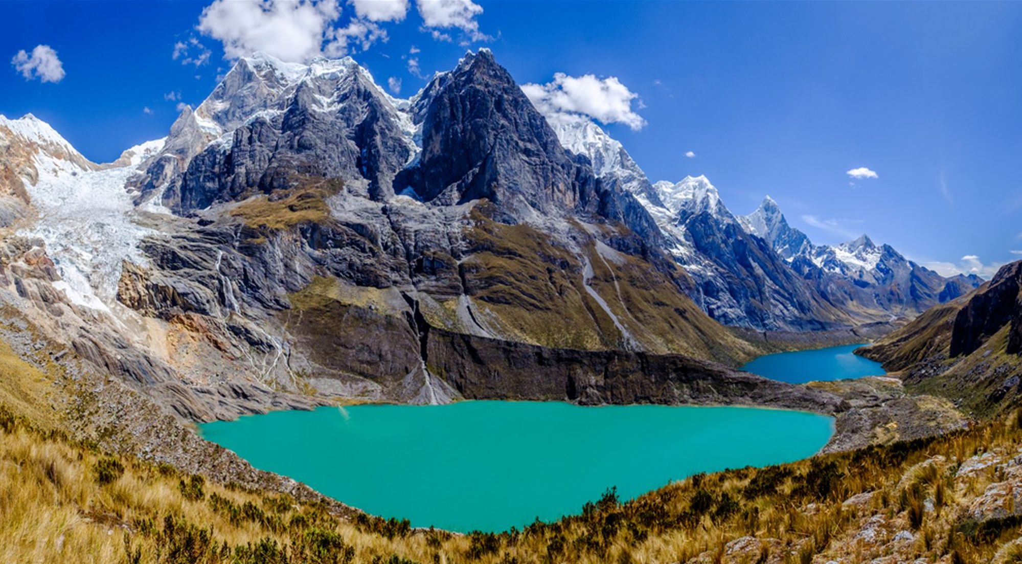 Turquoise bergmeer in de Peruaanse Andes met besneeuwde bergtoppen onder een blauwe lucht.