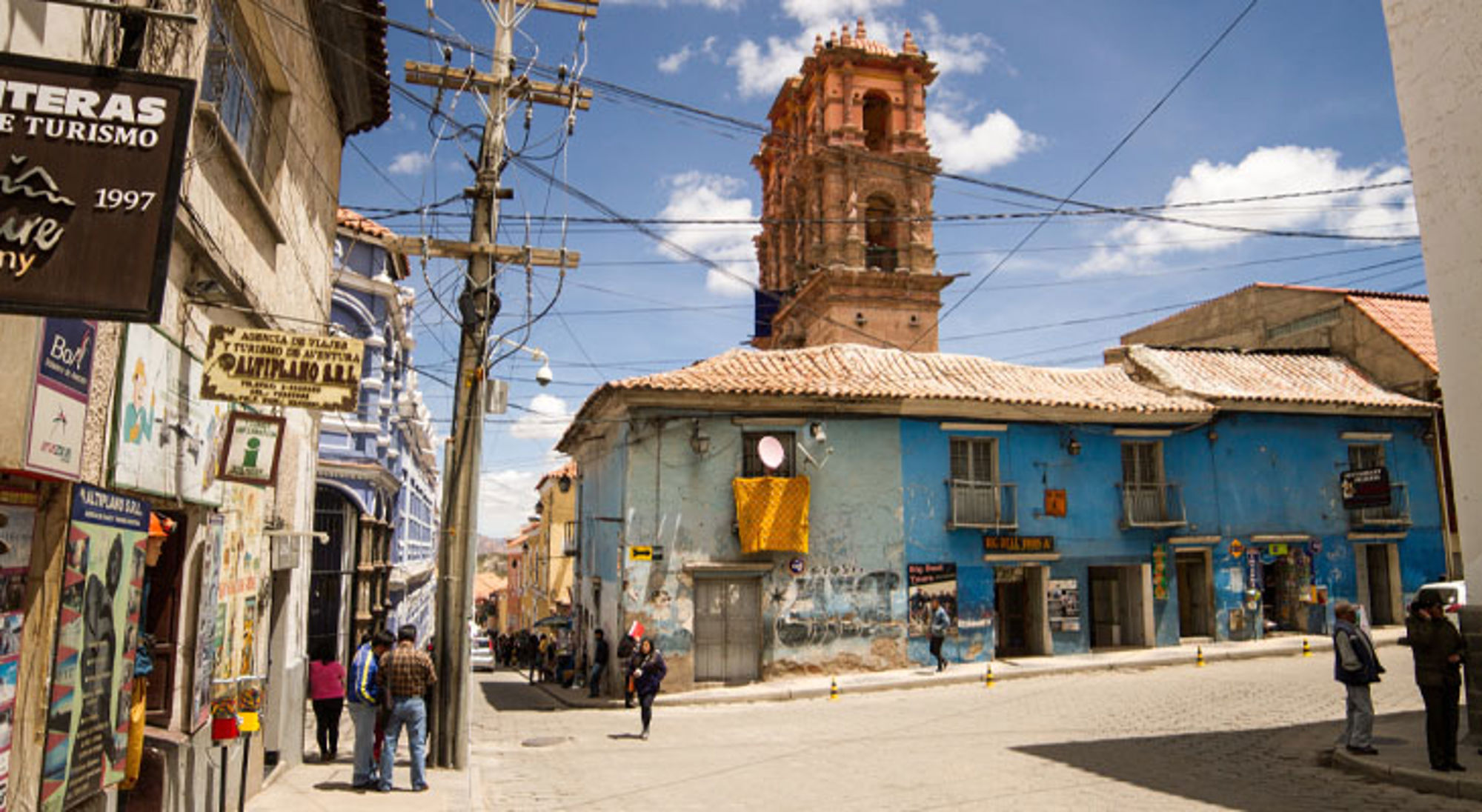 Straatbeeld in Potosí, Bolivia, met kleurrijke gebouwen en een historische kerktoren onder een blauwe lucht.