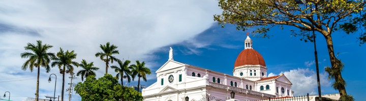 Witte kerk met rode koepel en palmbomen onder een blauwe lucht in Costa Rica.