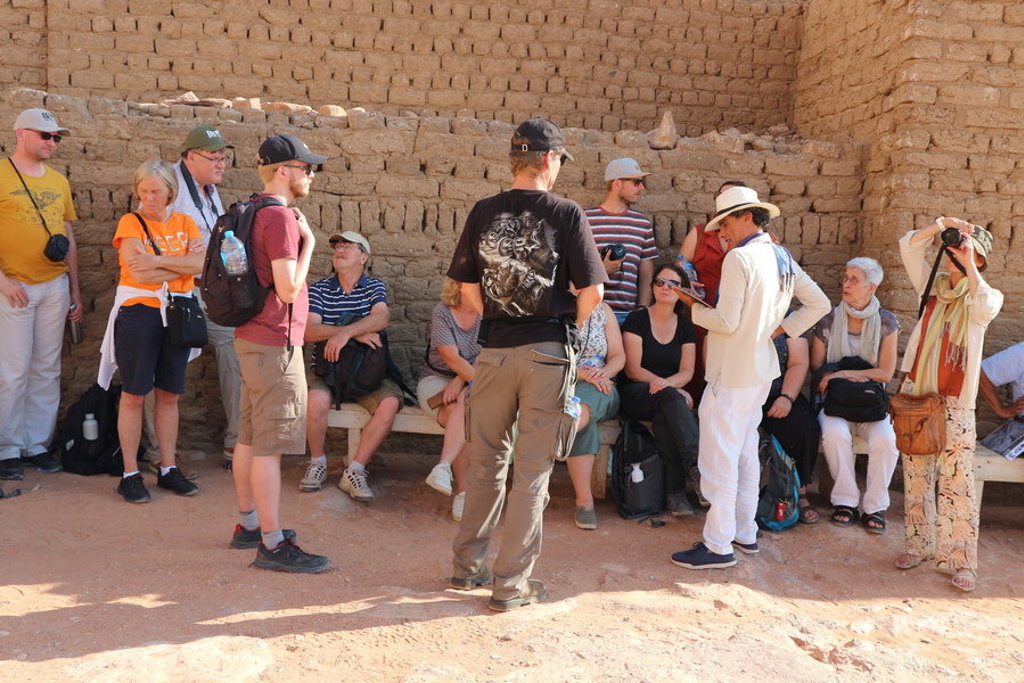 Groepsrondreis Egypte: reisleider geeft uitleg aan groep reizigers bij een historische lemen muur.