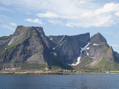 Berglandschap aan de kust van de Lofoten in Noorwegen, met steile rotswanden en sneeuwvelden onder blauwe lucht.