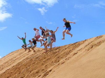 Groep reizigers springt van een zandduin tijdens de Route Vietnam-reis, met blauwe lucht op de achtergrond.