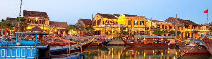 Verlichte oude stad Hoi An met boten aan de rivier in Vietnam bij schemering.