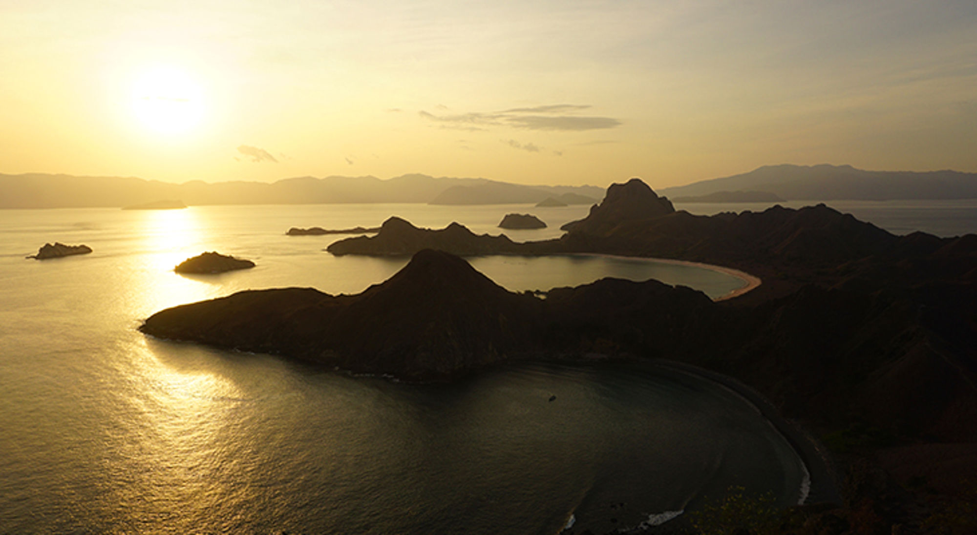 Zonsondergang boven de Komodo-eilanden met bergachtige kustlijn en baaien, Indonesië.
