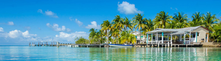 Palmbomen, houten huisjes en steiger aan een rustige lagune in Belize.