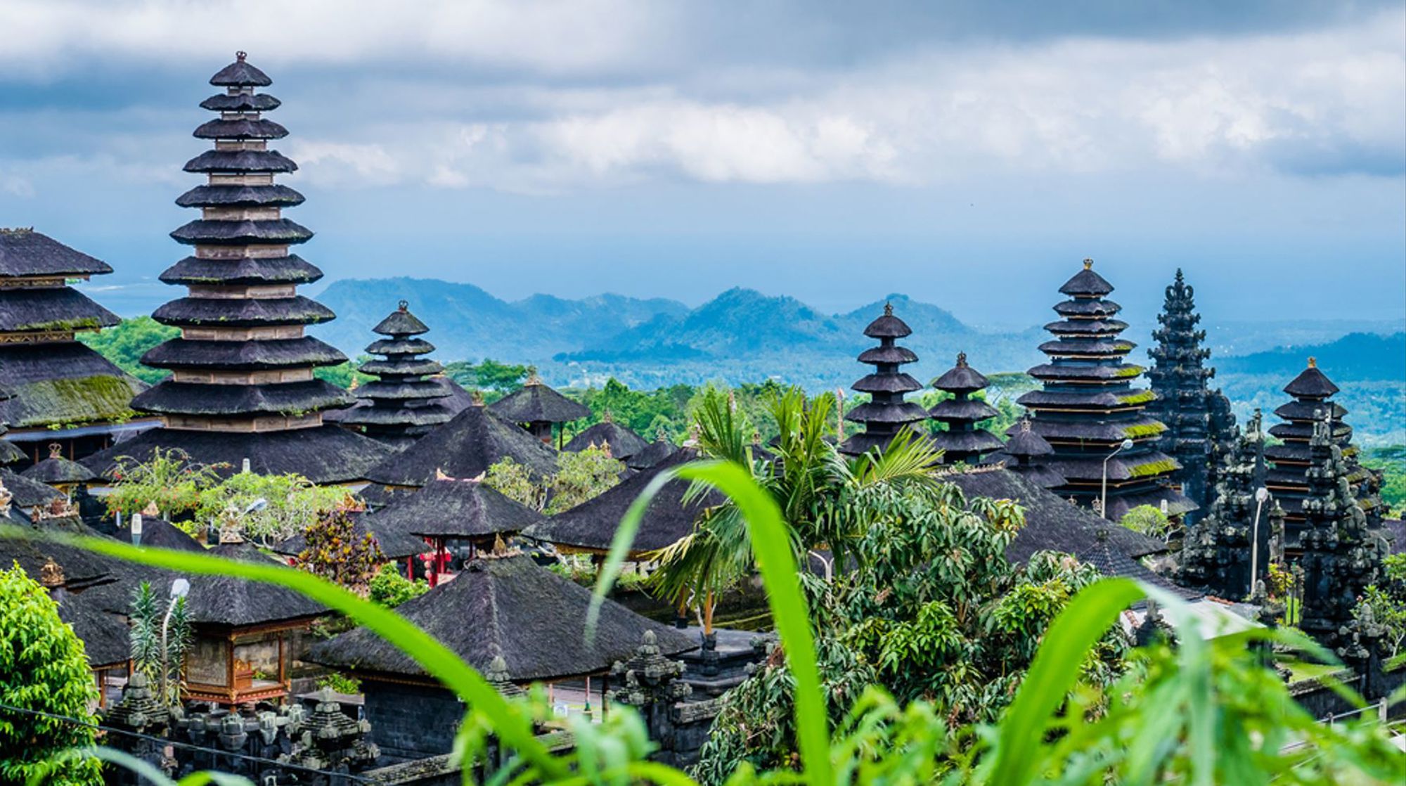 Balinese tempelcomplex met meru-torens en groene heuvels op de achtergrond, Indonesië.
