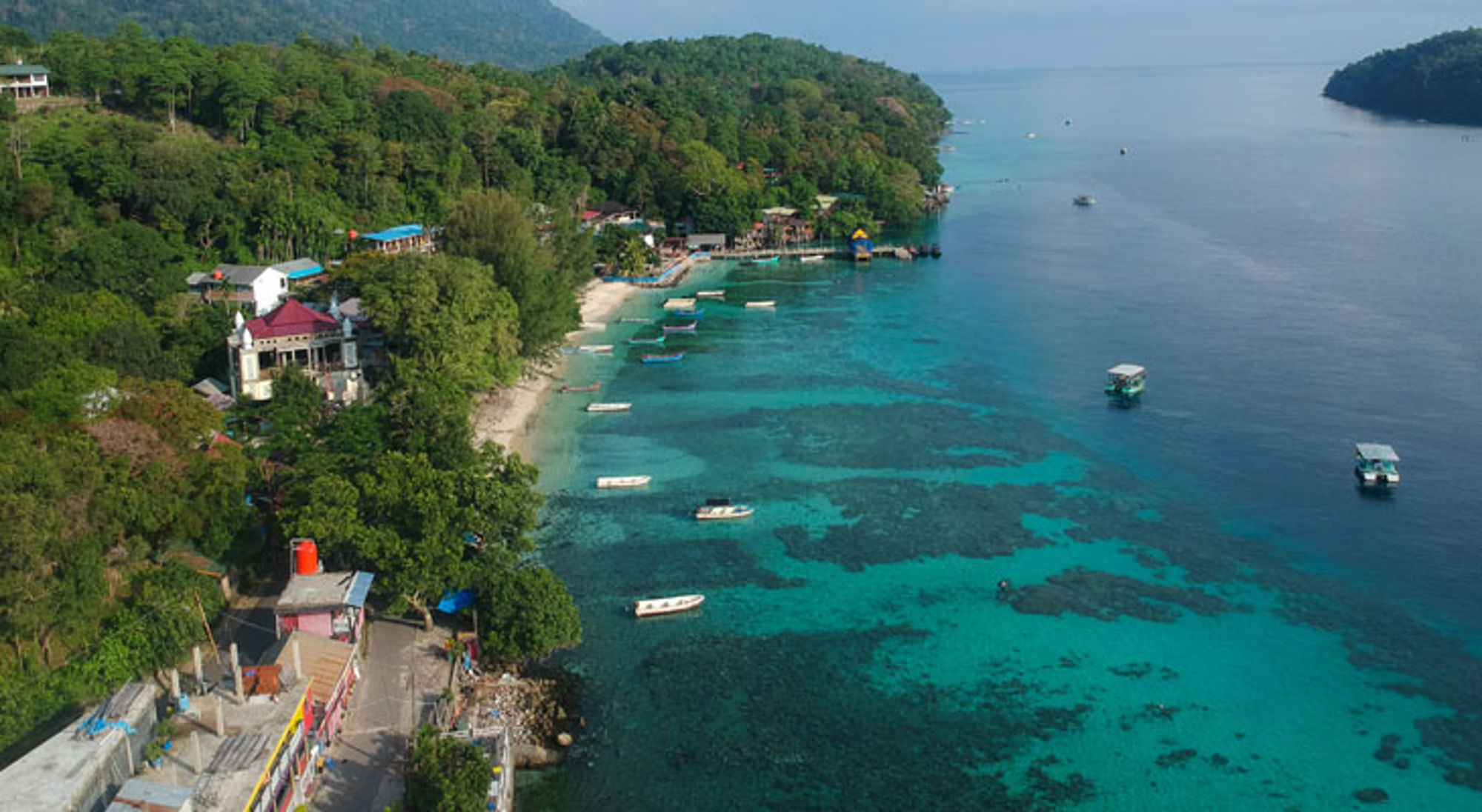 Iboih Indonesië een tropische kust in Indonesië met turquoise zee, koraalriffen en boten langs het strand.